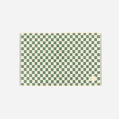 Bath mat with green and cream checkerboard pattern, small label on corner.