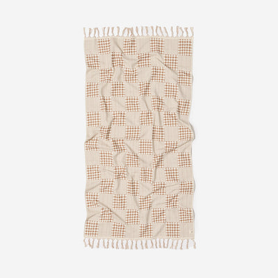 Checkered beige and brown sand resistant towel with fringed edges, flat on surface.