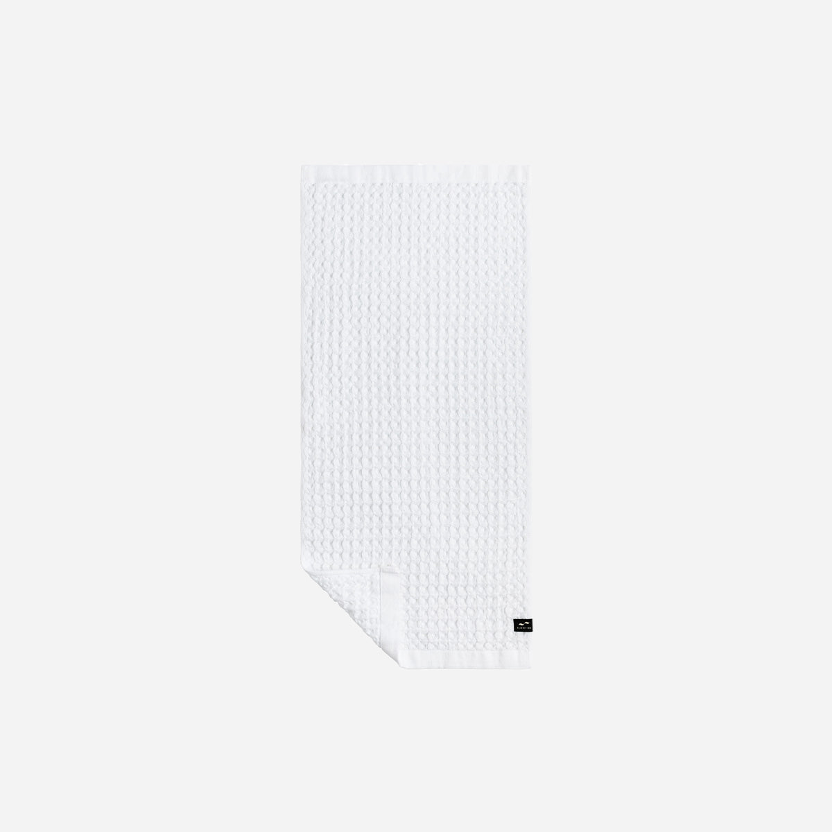White waffle bath towel with black label detail on a plain light background.