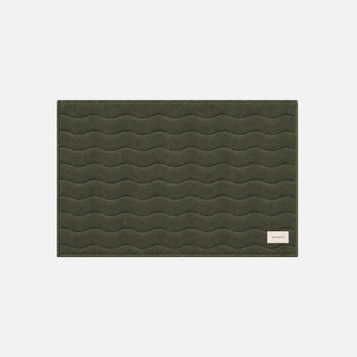 Dark green bath mat with wavy stitch pattern and small white label in one corner.