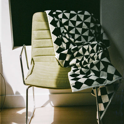 Geometric pattern blanket with bold shapes displayed on a beige chair in natural light.