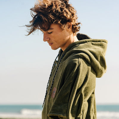 Green extra-warm towel poncho with hood, soft terry material, beach setting.