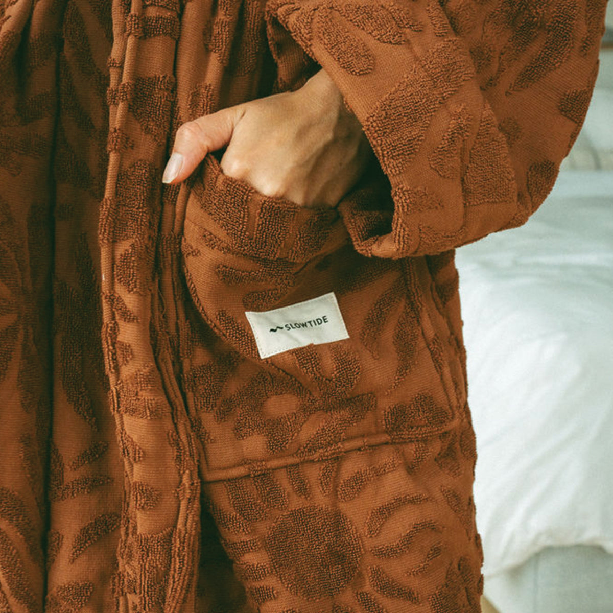 Plush terry cloth robe in brown with textured floral pattern and front pocket.