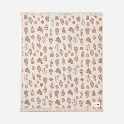 Beige oversized blanket with brown shell and rock pattern, fringed edges, small white tag.