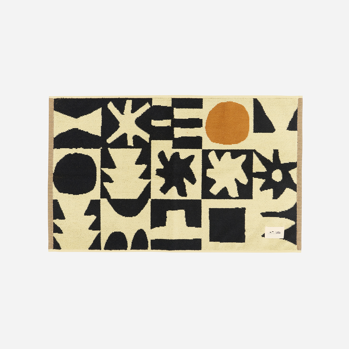 Bath mat with absorbent material and black and orange abstract shapes on cream background.