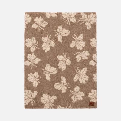 Tan area rug with cream leaf pattern, shown with a cozy throw for comfort.