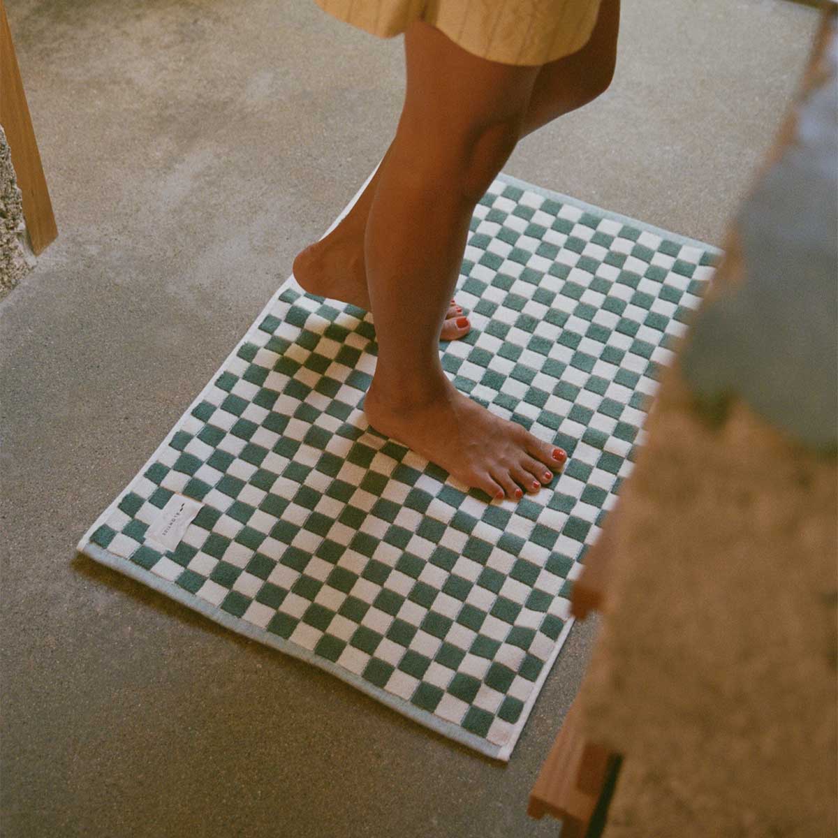 Checkerboard bath mat with green and white pattern on concrete floor.