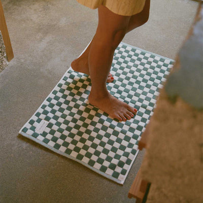 Checkerboard bath mat with green and white pattern on concrete floor.