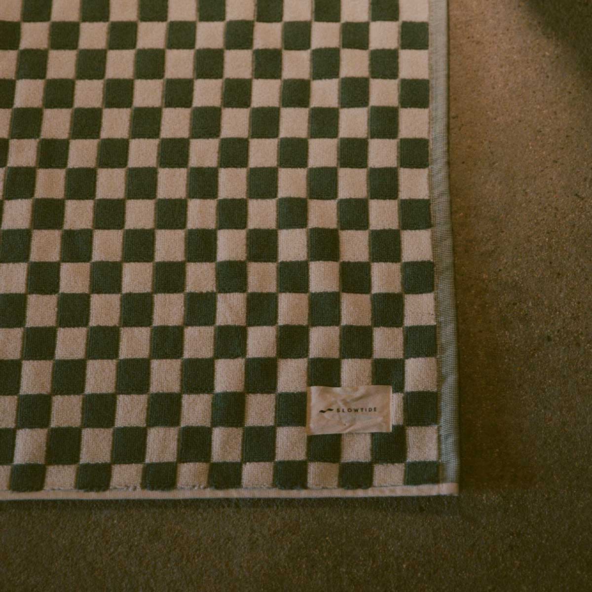 Cotton bath mat with checkerboard pattern and small tag on corner.