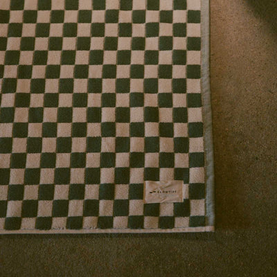 Cotton bath mat with checkerboard pattern and small tag on corner.