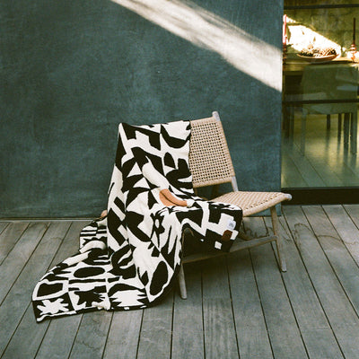 Woven chair with abstract patterned throw blanket on wooden deck.