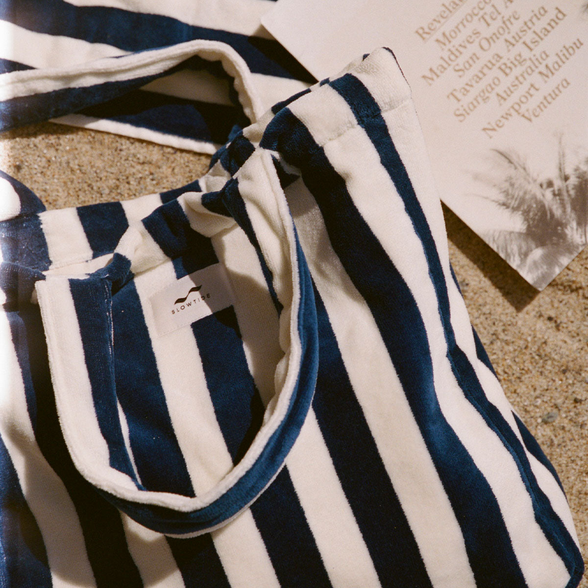 Striped blue and white canvas tote bag with handles on sand.