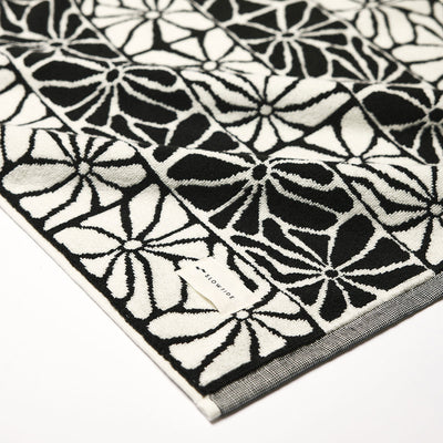 Black and white towel with geometric floral pattern and small label, highly absorbent cotton.
