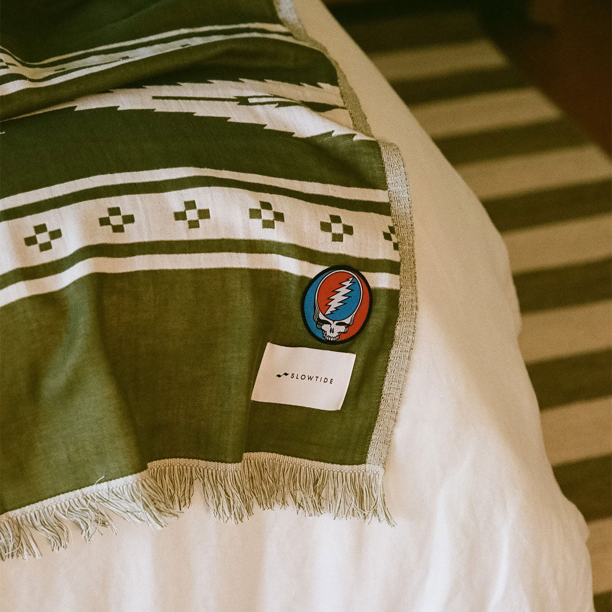 Green patterned blanket with driftweave texture on bed, striped rug visible below.