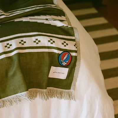 Green patterned blanket with driftweave texture on bed, striped rug visible below.