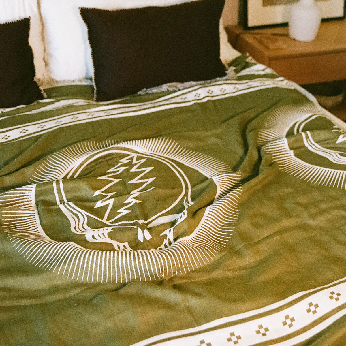 Bedspread, green with white patterns, includes two dark pillows.