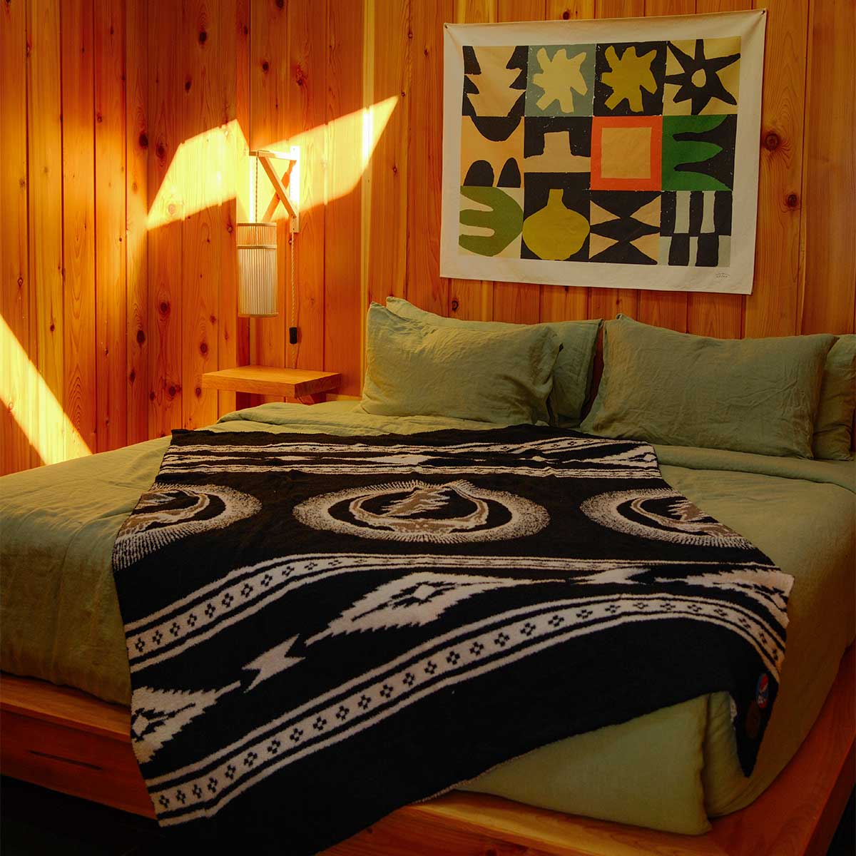 Woven throw blanket with Grateful Dead pattern on olive green bedding.