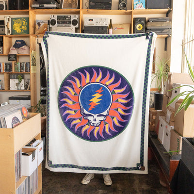 Fleece throw blanket featuring a skull and sun graphic with a checkered border.