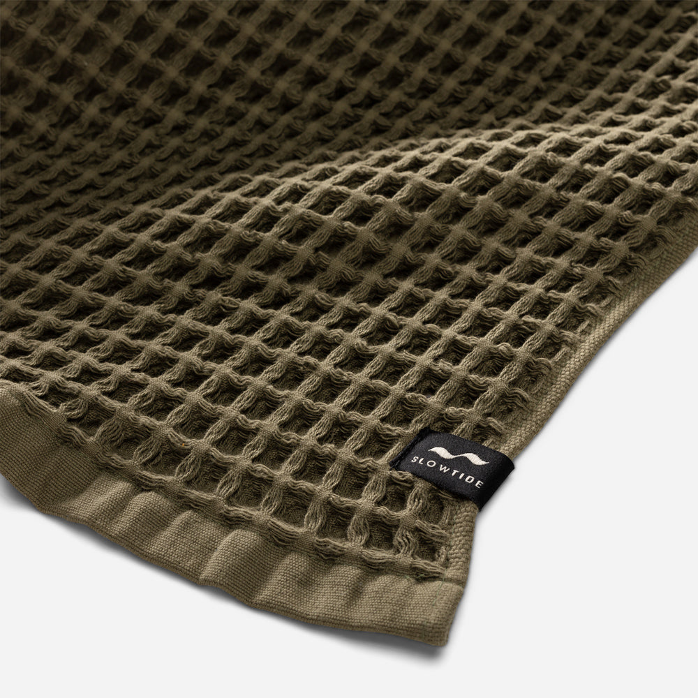 Waffle towel in olive green with textured pattern and small tag attached.