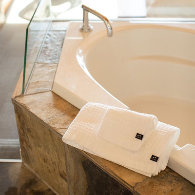 Absorbent cotton towels folded on a stone bathtub near a silver faucet.