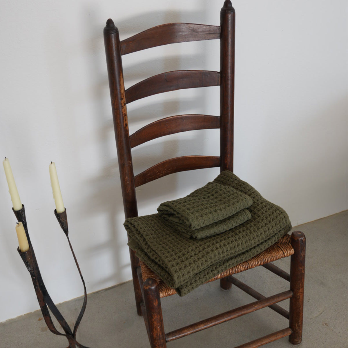 Cotton towels folded on wooden chair next to metal candle holder with two candles.