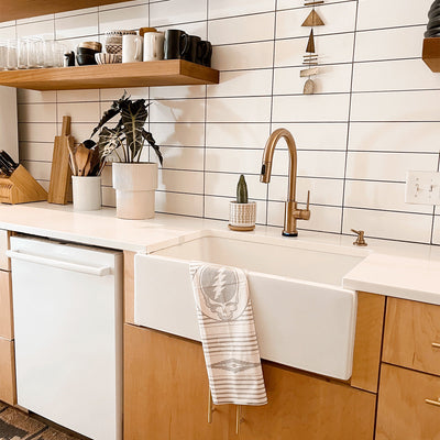 Kitchen towel with colorful graphic on open shelf in modern kitchen with farmhouse sink.