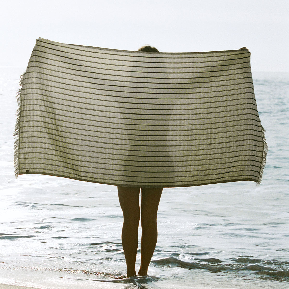 Turkish towel with green stripes and frayed edges at the ocean.