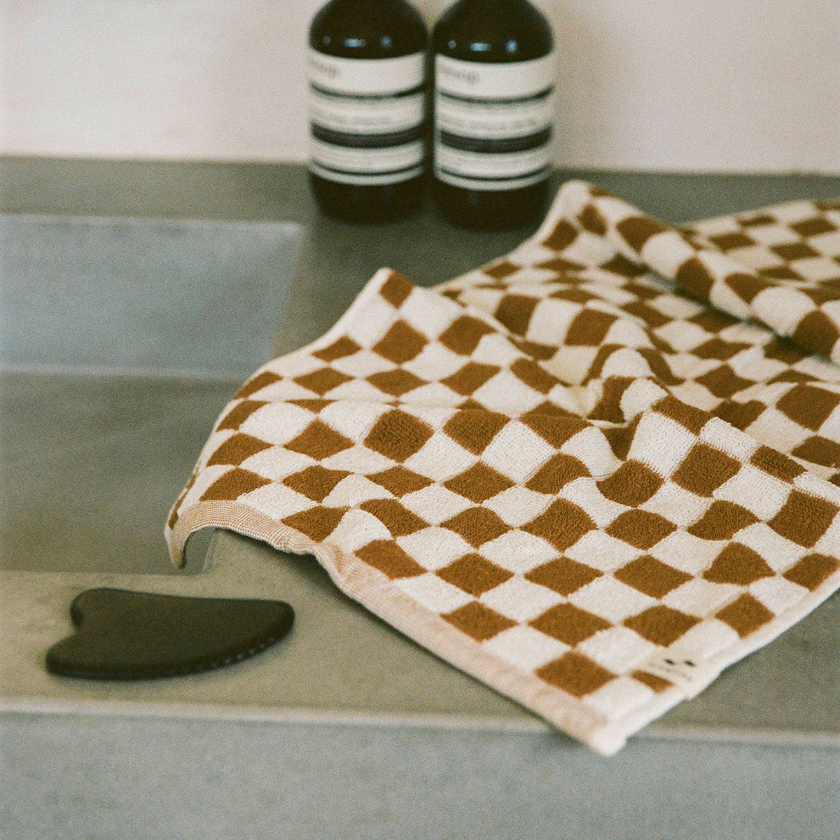 Hand towel, absorbent brown and white checkerboard weave, shown on gray counter with bottles.