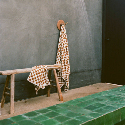 Wooden bench with absorbent towels near green-tiled shower area.