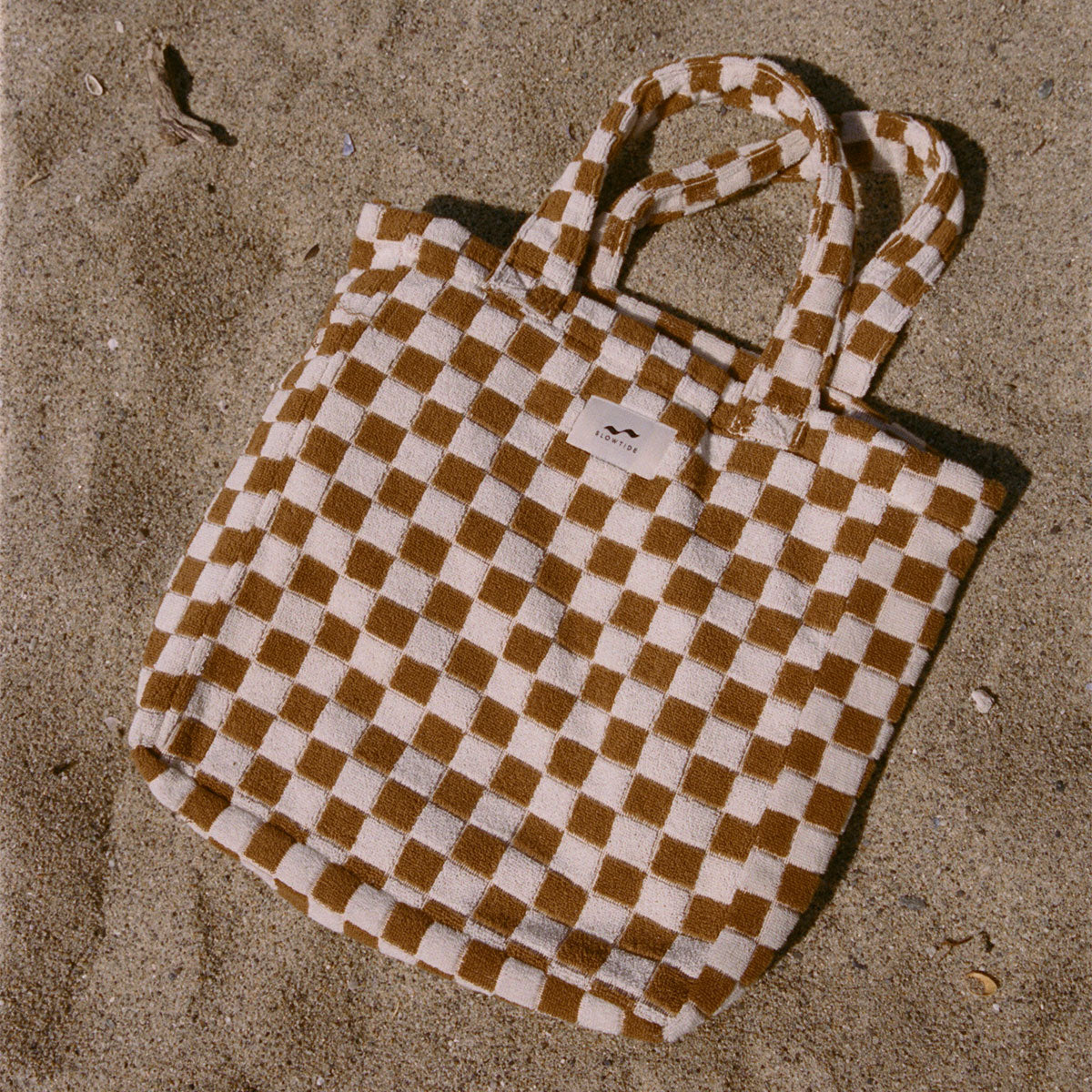 Beach bag with vintage checkered pattern on sand.