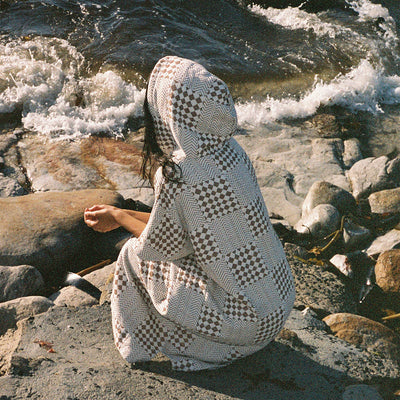 Surf poncho in brown and white checkered sustainable cotton by the water.