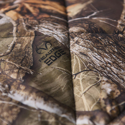 Quilted packable blanket with photorealistic camo print and stitched logo detail.
