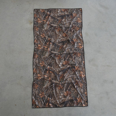 Camo quick-dry towel with brown and green leaf pattern on grey floor.