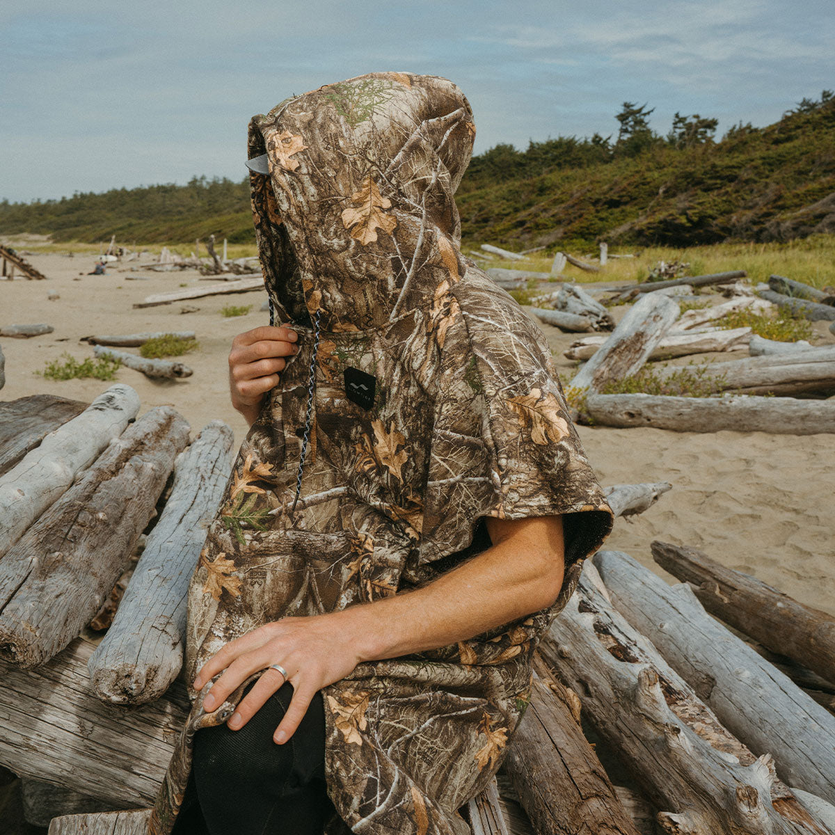Hooded poncho with camouflage pattern on driftwood logs at beach.