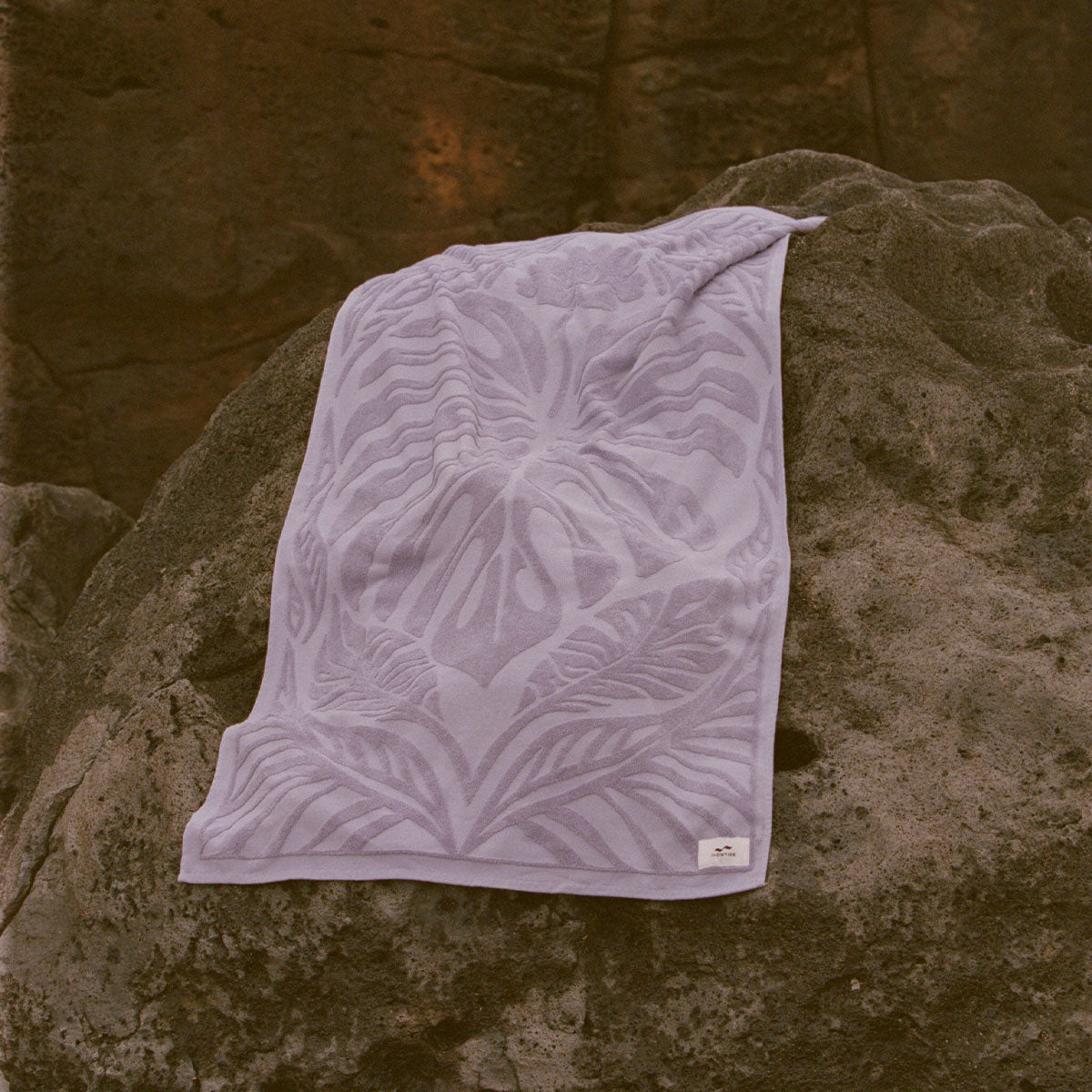 Lavender cotton velour towel with raised leaf pattern on a rock.
