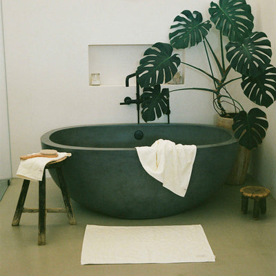 Oval bathtub with dark finish and plush cotton towels in a modern bathroom setting.