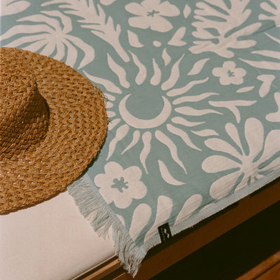 Straw sunhat on Turkish towel with blue and white sun and floral pattern.
