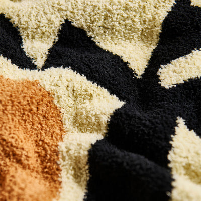 Knit throw blanket with plush texture and black, beige, and brown abstract pattern.