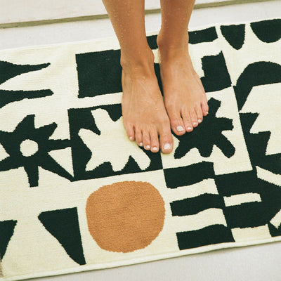 Bath mat with abstract black shapes and brown circle on cream background.